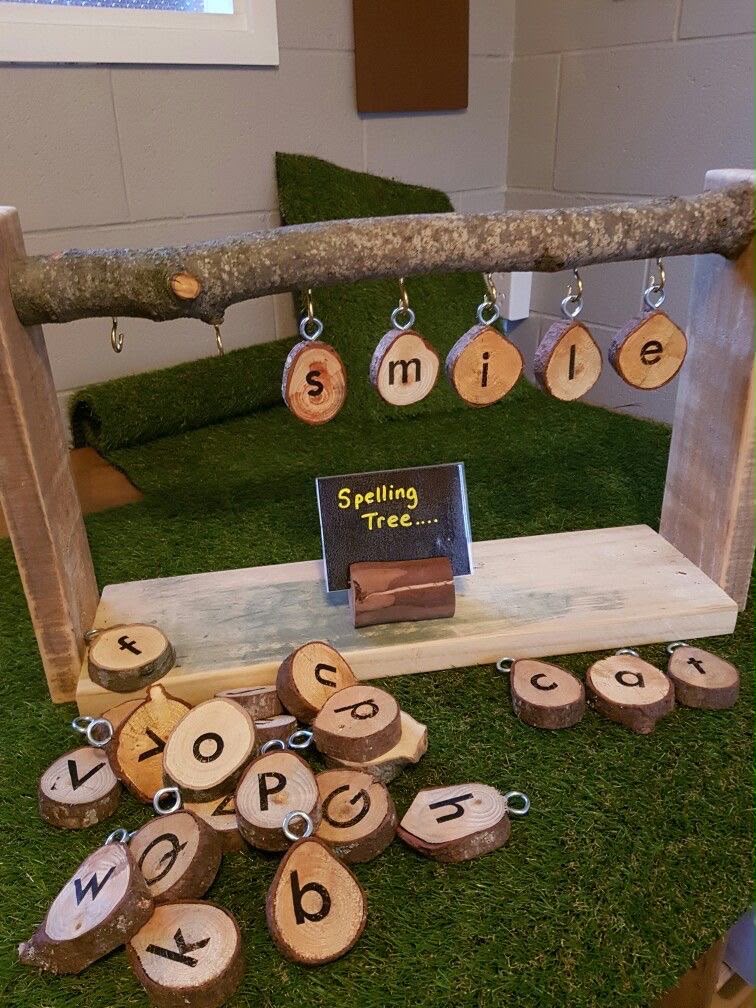 A branch on a stand with hanging wooden letter discs spelling the word smile